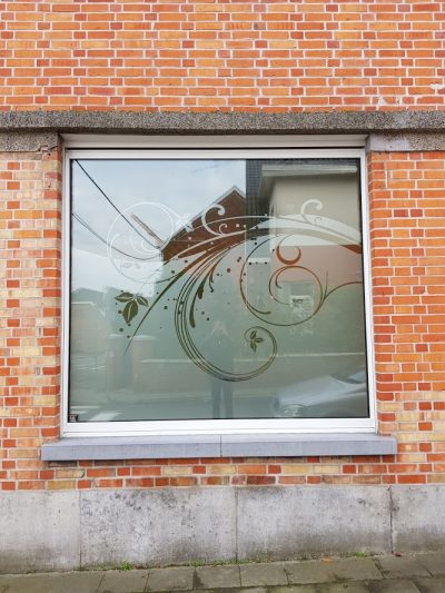 Fenêtre d'une façade en briques rouges avec un film à effet sablé à grand motif floral en volutes