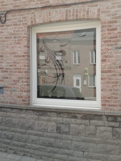 Fenêtre d'une façade en briques claires avec un film à motif végétal en volutes dans l'angle du vitrage