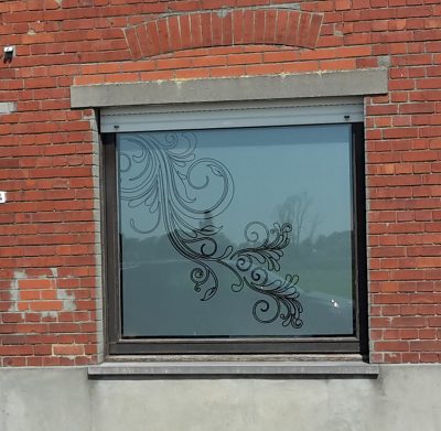 Fenêtre d'une façade en briques rouges avec un film à effet sablé ajouré d'une arabesque de feuillages en volutes