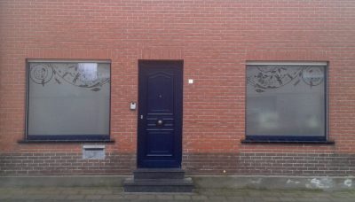 Deux fenêtres d'une façade en briques rouges de part et d'autre d'une porte bleue, avec un film à effet sablé à motif de libellules et de fleurs