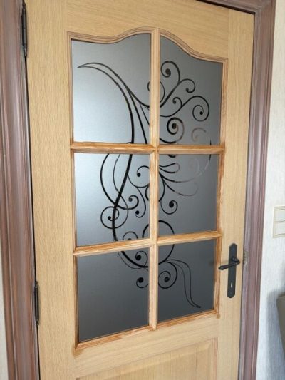 Porte intérieure en bois clair à six carreaux dont le vitrage porte un film à effet sablé ajouré de grandes volutes et de spirales