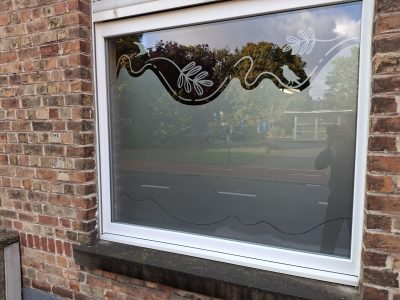Fenêtre d'une façade en briques rouges avec un film à effet sablé en frise ondulée de feuillage et d'oiseaux
