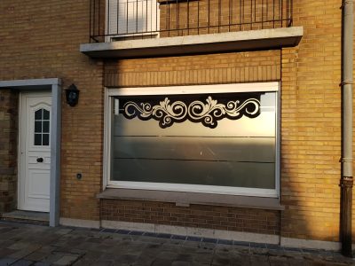 Fenêtre d'une façade en briques jaunes avec un film à effet sablé bordé en haut d'une frise de volutes et traversé de deux fines bandes claires