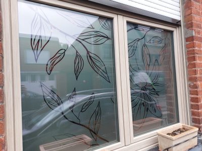 Fenêtre à deux vantaux d'une façade en briques rouges dont le vitrage porte un film adhésif sombre découpé en feuillages et en grande fleur de lys