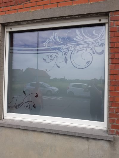 Grande fenêtre d'une façade en briques rouges dont le vitrage porte un film à effet sablé ajouré de volutes feuillues et de deux lignes horizontales