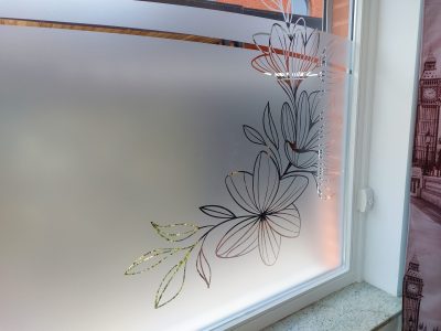 Fenêtre à châssis blanc vue de l'intérieur avec un film à effet sablé ajouré de grandes fleurs stylisées au trait et de feuilles