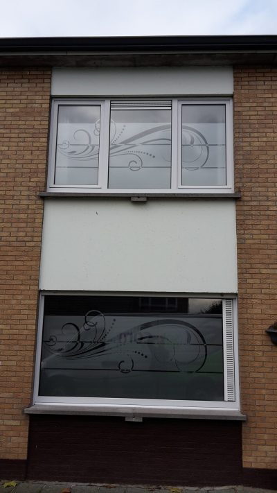 Deux fenêtres superposées d'une façade en briques dont le vitrage porte une bande de film à effet sablé ajourée de volutes et de pointillés