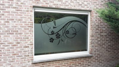 Grande fenêtre à châssis blanc d'une façade en briques avec un film à effet sablé au bord en vague, orné de volutes et de fleurs découpées en noir