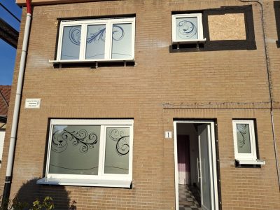 Fenêtres d'une façade en briques beiges avec un film à effet sablé à bord ondulé en partie basse, surmonté de grandes volutes sombres