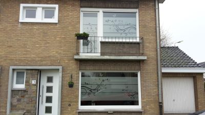 Deux fenêtres d'une façade en briques claires dont le vitrage porte un film à effet sablé à motif de volutes fleuries et de papillons