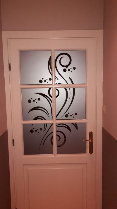 Porte intérieure blanche à six carreaux dont le vitrage porte un film à effet sablé ajouré d'une arabesque de vrilles, de spirales et de bulles courant sur toute la hauteur