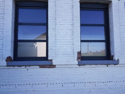 Deux fenêtres d'une façade en briques peintes en blanc avec un film à effet sablé à fines lignes et losange
