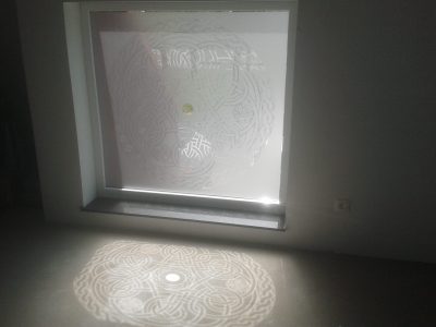 Film à effet sablé à motif d'entrelacs celtiques sur une fenêtre, le motif se projette en ombre sur le sol