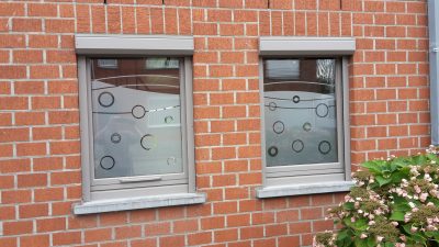 Deux fenêtres d'une façade en briques rouges avec un film à effet sablé à motif de cercles et d'anneaux