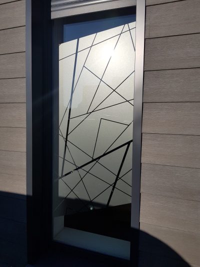 Fenêtre étroite d'une façade en bardage, film à effet sablé traversé de lignes droites entrecroisées