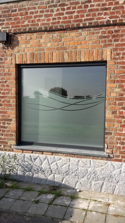 Fenêtre fixe d'une façade en briques rouges avec un film à effet sablé à motif de lignes ondulées