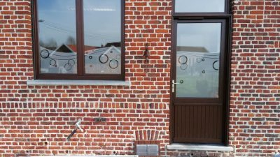 Fenêtre et porte vitrée d'une façade en briques rouges avec un film à effet sablé à motif de cercles de tailles variées