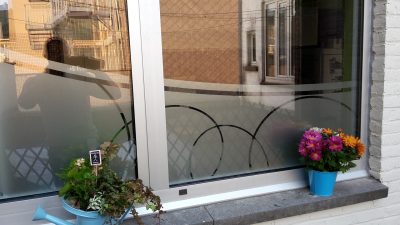 Fenêtre d'une façade blanche avec un film à effet sablé à motif de grands arcs de cercle, pots de fleurs sur l'appui