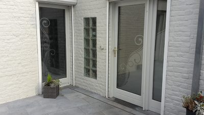 Fenêtre et porte vitrées d'une façade en briques peintes en blanc avec un film à effet sablé à motif de volutes