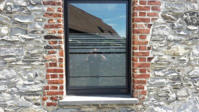 Fenêtre d'une façade en pierre et briques avec un film à effet sablé à bandes horizontales et petits losanges