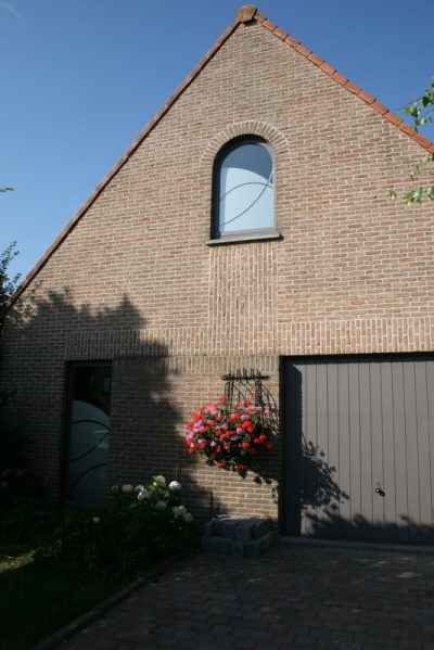 Pignon en briques d'une maison avec un film à effet sablé à motif de courbes sur la fenêtre cintrée et sur la porte d'entrée