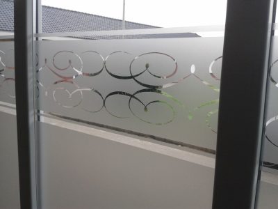 Garde-corps vitré d'une terrasse avec un film à effet sablé ajouré d'une frise de volutes, toits de tuiles en arrière-plan