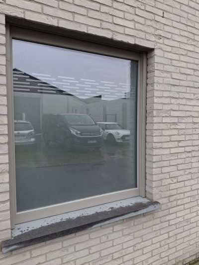 Fenêtre carrée d'une façade en briques blanches dont la partie haute du vitrage porte un film à effet sablé à motif de tirets horizontaux en quinconce