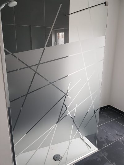 Paroi fixe de douche dans une salle de bains au carrelage anthracite, couverte d'un film à effet sablé ajouré de lignes droites de largeurs variées qui s'entrecroisent