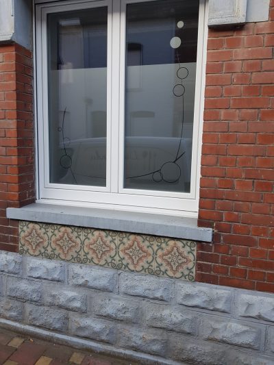 Fenêtre à deux vantaux d'une façade en briques rouges dont les vitres portent un film à effet sablé à motif de bulles reliées par de fins traits courbes