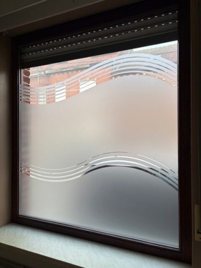 Fenêtre à cadre brun foncé sous un volet roulant, dont le vitrage porte un film à effet sablé dégagé en haut et ajouré de deux vagues en fines bandes transparentes