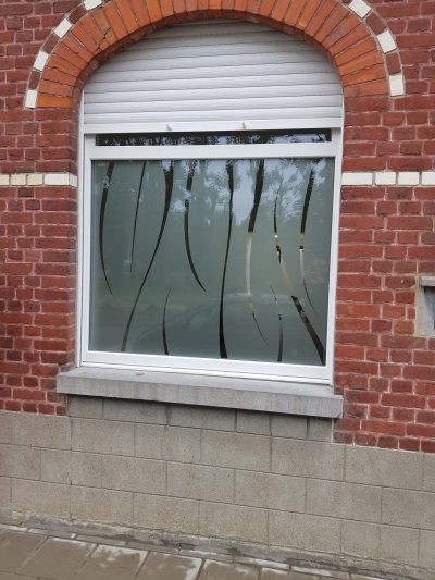 Fenêtre d'une façade en briques rouges avec un film à effet sablé ajouré de longues courbes élancées