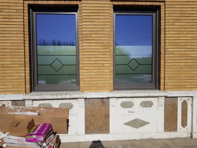 Deux fenêtres à châssis brun d'une façade en briques jaunes avec un film à effet sablé ajouré de lignes horizontales et d'un losange central