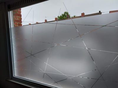 Fenêtre à châssis blanc dont le vitrage porte un film à effet sablé ajouré de fines lignes droites entrecroisées