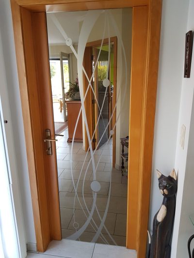 Porte intérieure vitrée à cadre en bois clair dont le vitrage porte un film à effet sablé découpé en courbes entrelacées et en disques
