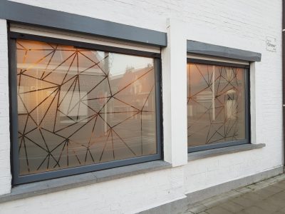 Deux fenêtres d'une façade en briques peintes en blanc dont le vitrage porte un film à effet sablé ajouré d'un réseau de lignes fines formant des triangles