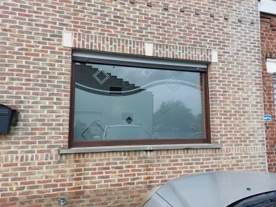 Grande fenêtre à châssis brun d'une façade en briques rouges avec un film à effet sablé à motif de bande ondulée et de losanges