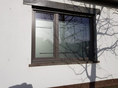 Fenêtre à deux vantaux au châssis anthracite d'une façade crépie blanche avec un film à effet sablé à fines lignes horizontales
