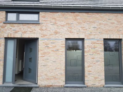 Deux hautes fenêtres et une petite fenêtre au-dessus de la porte d'entrée d'une façade en briques claires avec un film à effet sablé ajouré de carrés arrondis imbriqués