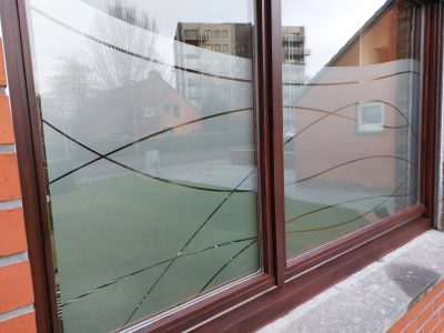 Fenêtre à deux vantaux au châssis acajou dans une façade en briques rouges, dont le vitrage porte un film à effet sablé ajouré de vagues entrecroisées
