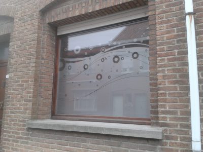 Fenêtre d'une façade en briques rouges au châssis brun dont le vitrage porte un film à effet sablé ajouré d'anneaux et de bulles le long de courbes ondulantes