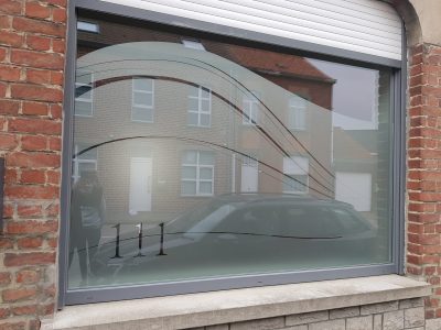 Grande fenêtre d'une façade en briques rouges avec un film à effet sablé ajouré de courbes élancées et du numéro de la maison