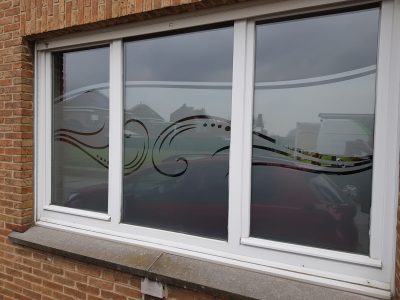 Fenêtre à trois vantaux d'une façade en briques rouges avec un film à effet sablé ajouré d'une vague de volutes et de points