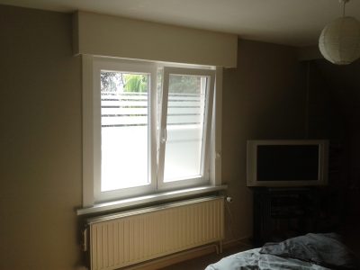 Fenêtre blanche à deux vantaux d'une chambre dont le vitrage porte un film à effet sablé plein en partie basse, terminé en haut par des bandes horizontales de plus en plus fines