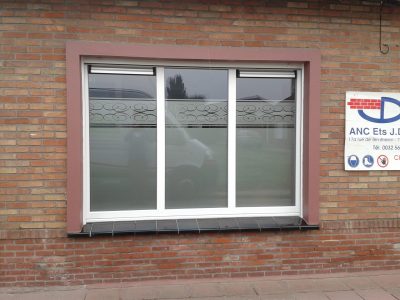 Fenêtre à trois vantaux d'une façade en briques rouges dont le vitrage porte un film à effet sablé bordé d'une frise de volutes ajourées