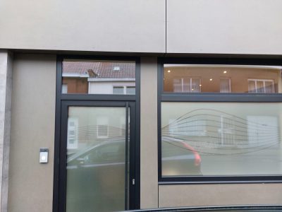 Porte d'entrée vitrée et fenêtre à châssis noirs d'un bâtiment moderne, dont le bas des vitrages porte un film à effet sablé parcouru de fines lignes ondulées