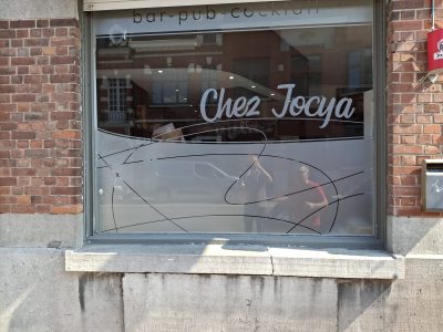 Vitrine d'un bar en façade de briques rouges avec un film à effet sablé portant le nom de l'établissement et des courbes fines entrecroisées