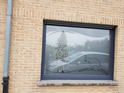 Fenêtre d'une façade en briques jaunes avec un film sur mesure représentant des palmiers et un éléphant