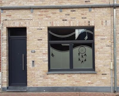 Fenêtre d'une façade en briques claires avec un film à effet sablé à motif d'attrape-rêves et de plumes suspendues à des courbes