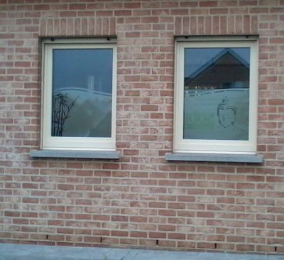Deux fenêtres d'une façade en briques avec un film à effet sablé à motif de bambou et de visage de bouddha