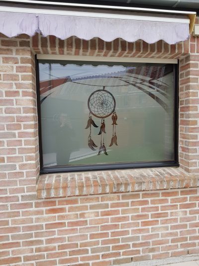 Grande fenêtre à châssis noir d'une façade en briques avec un film à effet sablé à motif d'attrape-rêves à plumes suspendu à de grandes courbes